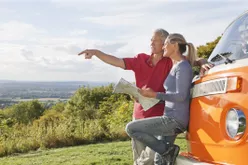 Older couple looking at map by a camper van and enjoying their retirement.